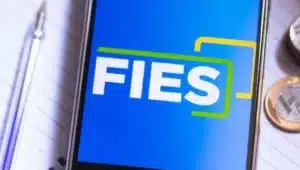 celular com app do fies ao lado de caneta e moedas e em cima de caderno